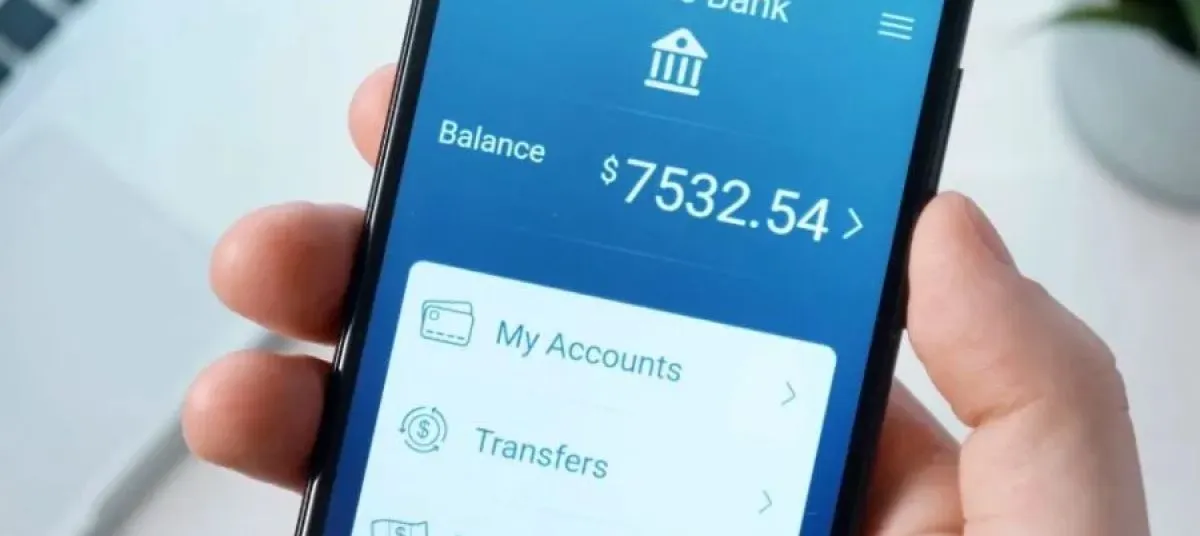 Hand holding a smartphone showing a mobile banking app balance.
