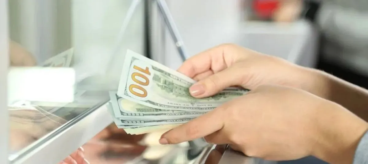 Hands counting notes at a bank counter, representing a cash deposit or initial bank funding.